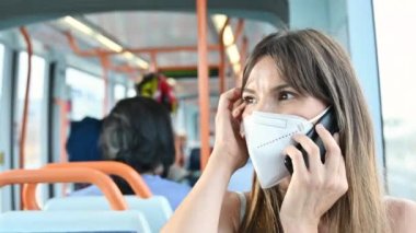 Yüz koruyucu maskeli genç bir kadın telefonda konuşuyor, toplu taşıma araçlarına biniyor. Şehir treninde pencere kenarında oturan maskeli kadın..