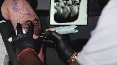 Ağır çekimde dövmeci alayının yakın görüntüsü. Usta profesyonel dövme makinesiyle hatlar çiziyor. Yüksek kalite Tam HD görüntü