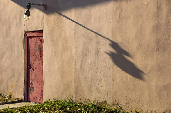 Duvarda eski yontulmuş kırmızı kapı. Bir fenerden bir gölge.