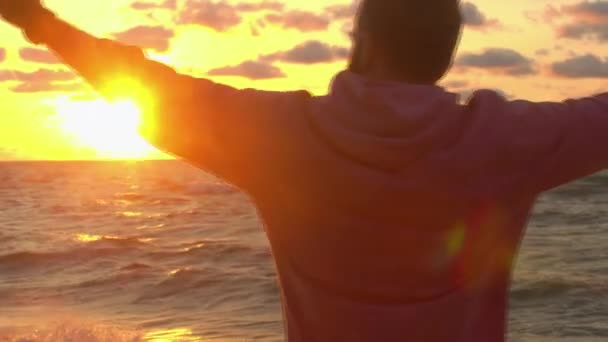 The guy raises his hands on the sea on the background of the sunrise — Stock Video