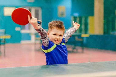 Tenis koridorda duran, elleri iki yanda yayılan neşeli mutlu bir çocuk. Tenis salonu, tenis raketi, Masa Tenisi