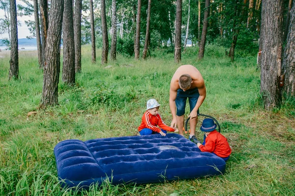 男人带着孩子在树林里抽着蓝色的气垫床垫 — 图库照片