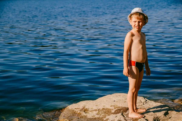 Cute Chłopiec Pięciu Lat Kąpielówki Stoi Duże Skały Plaży Słoneczny — Zdjęcie stockowe