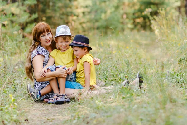 Jovem Avó Feliz Com Dois Netos Chapéus Sentados Gramado Floresta — Fotografia de Stock