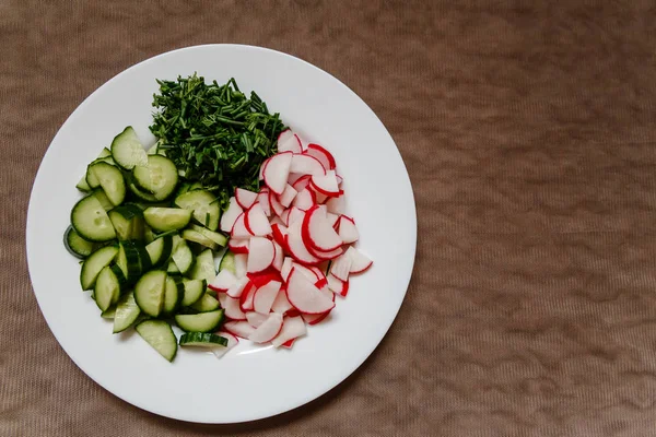 pieces of cucumber and fresh radish on a white plate, top view
