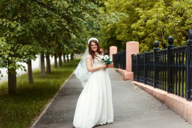 tam uzunlukta yaz aylarında parktaki kamera bakarak onun elinde bir buket ile beyaz elbise ve peçe güzel neşeli gelin