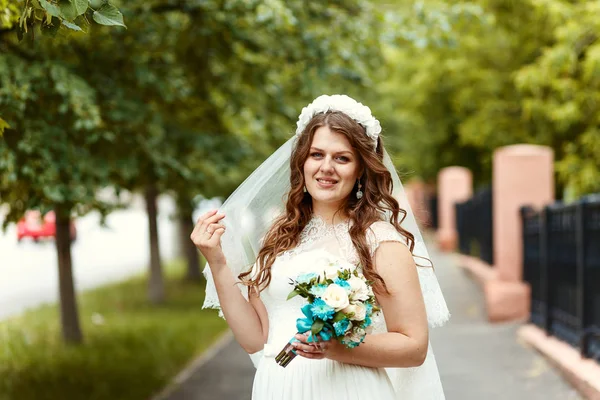 夏の公園でカメラを見て彼女の手で花束と白いドレスとベールの美しい陽気な花嫁 — ストック写真