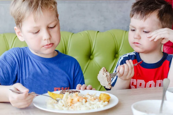 two little boys eating pasta with a cutlet from one plate