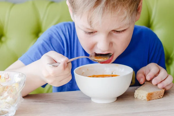 Маленький мальчик аппетитно ест вкусный суп большой ложкой — стоковое фото