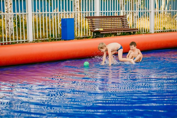 两个小滑稽的男孩在一个充气的室外游泳池里玩水上足球 — 图库照片