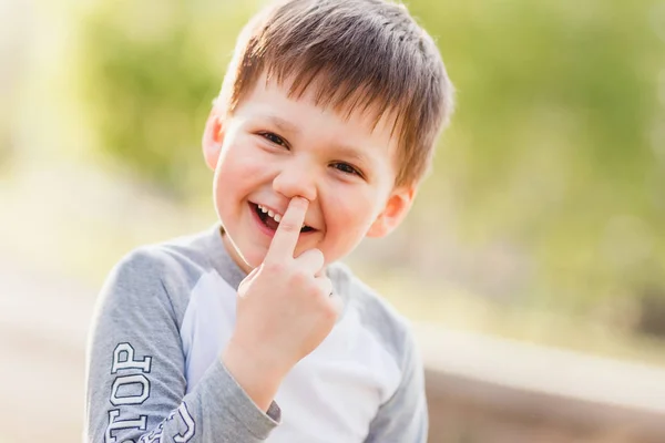 little funny boy picks his finger in the nose outdoors in summer