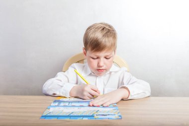 Beyaz gömlekli çocuk oturan bir resepsiyon ve beyaz bir arka plan üzerinde renkli kalemler boyama içinde berabere, birinci sınıftan