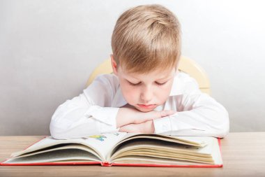 Beyaz arka plan üzerinde onun masasında bir kitapla oturan beyaz gömlekli çocuk