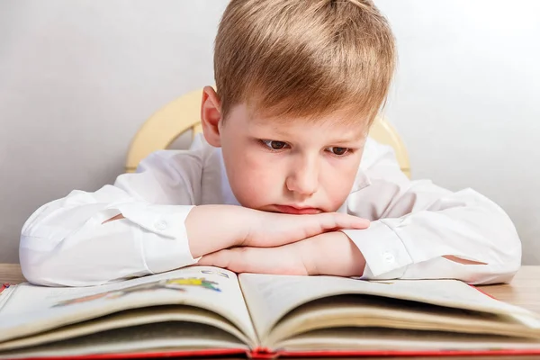 Üzgün çocuk masasında oturan ve bir kitap okuma beyaz gömlekli