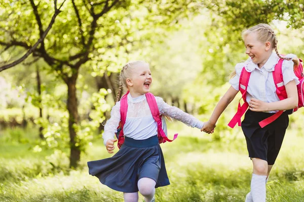 two funny school girls with school backpacks running holding hands outdoors