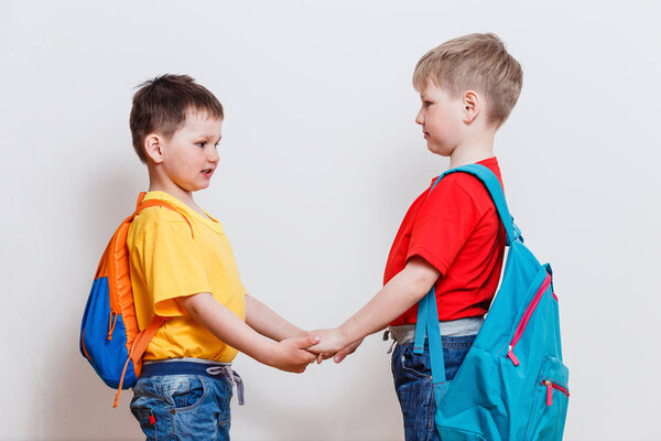 two boys with school backpacks holding hands on white background