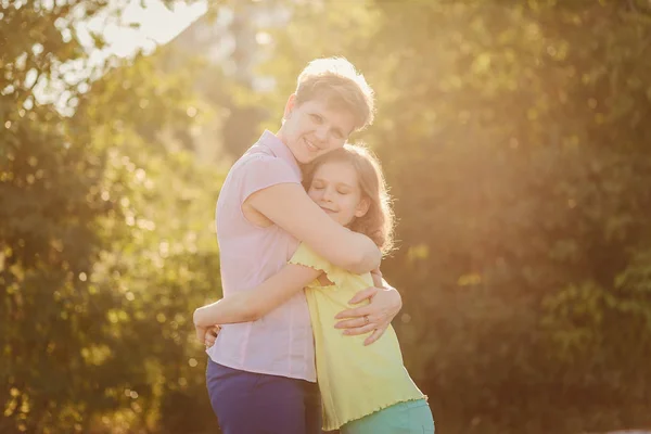 happy mom hugs daughter teen in backlight outdoors, happy family