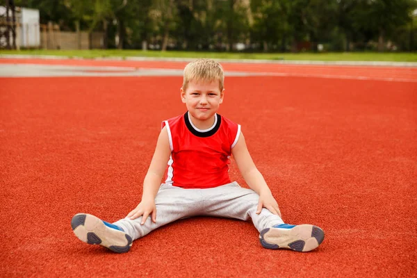 Здоровий Семирічний Хлопчик Спортивній Формі Сидить Червоній Поверхні Стадіону — стокове фото