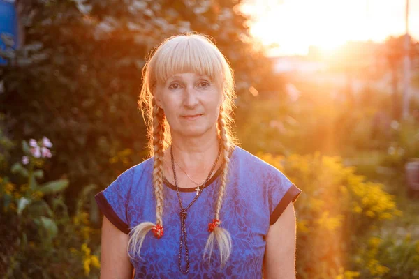 a woman of retirement age with two pigtails looking at the camera at the cottage at sunset