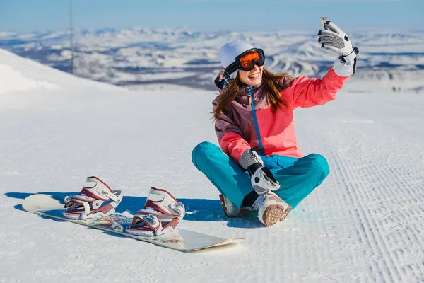 güzel kızla neşeli oturma ve selfies dağlarda alarak snowboard