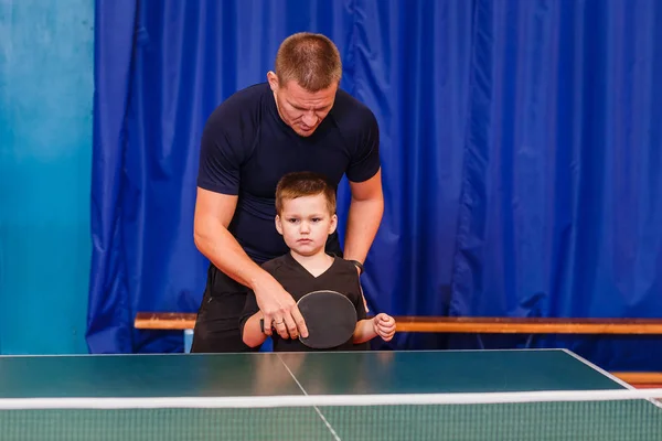 the coach teaches the child to play table tennis indoors