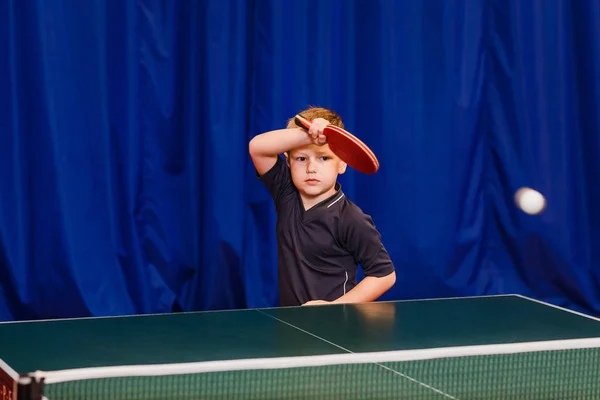 flying white ball in table tennis,a child plays table tennis indoors