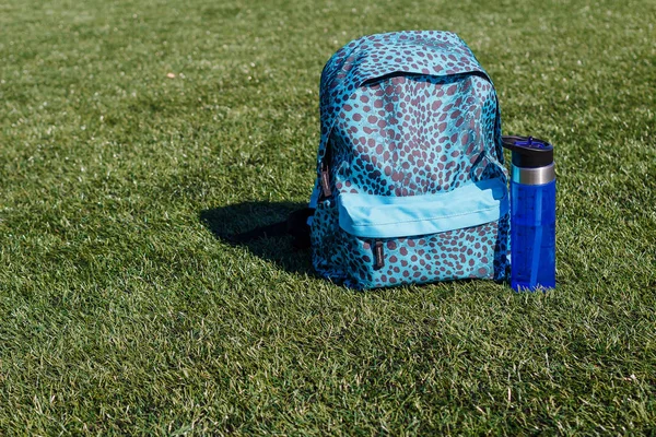 Sports backpack and water bottle on the grass outdoors