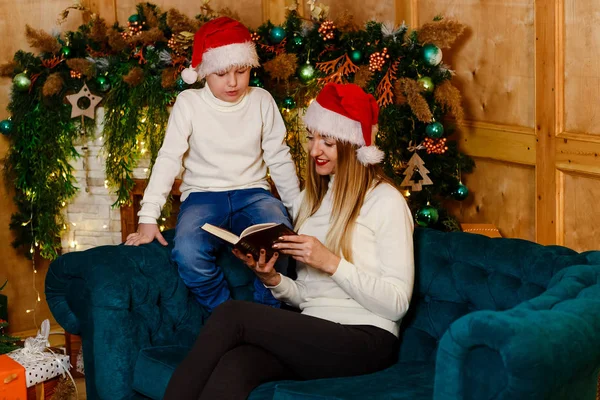 a young mother with her son reading a book for Christmas, mother and son in identical sweaters reading a book on the couch
