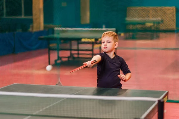 the blond boy plays table tennis in a specialized room. blurred background