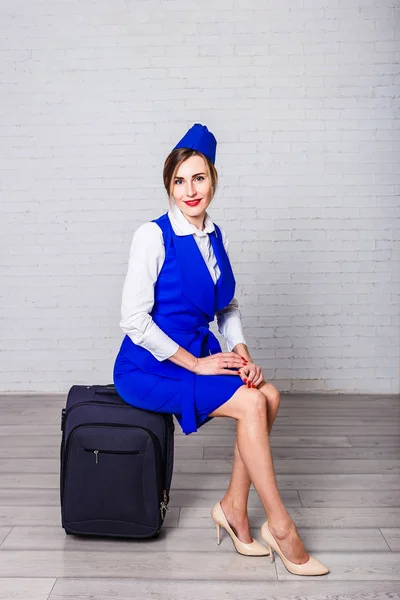 a young woman in a blue suit sitting on suitcase, a stewardess in a blue forage cap