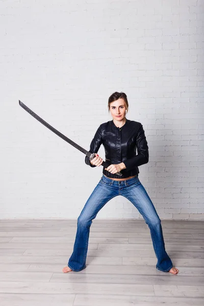 a young woman stands in a rack with a large sword in her hands on a white background .young woman in full height looking at camera on white background