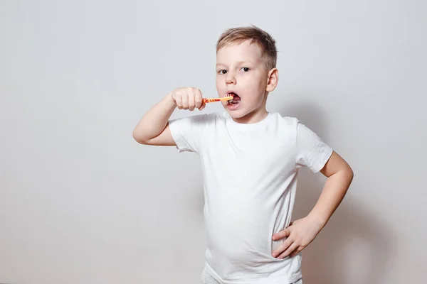 six-year-old boy in white t-shirt brushing his teeth on a white background