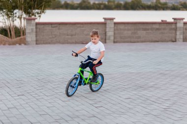 Yaz aylarında parkta kaldırım levhalar üzerinde bir bisiklet sürme beyaz bir t-shirt yedi yaşında çocuk