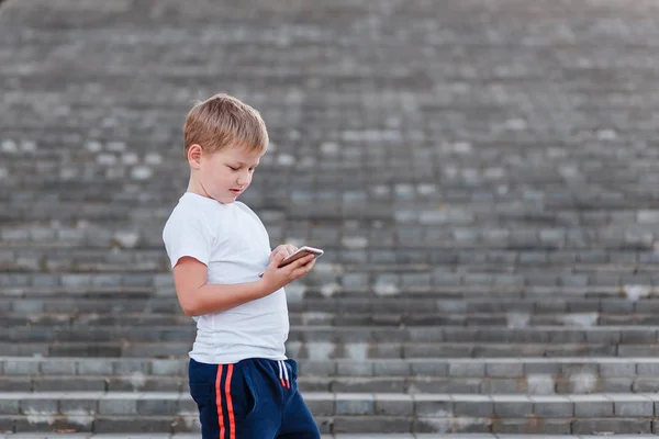 ヨーロッパだけで白い シャツを着た少年は 空気オープンに梯子にスマート フォンを楽しんでいます 子供とスマート フォン 子供とインターネット — ストック写真