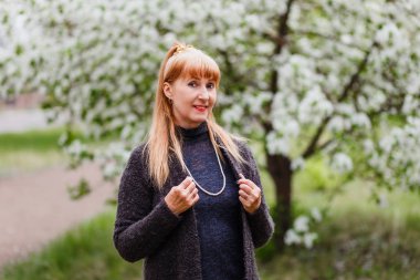 sarışın gülümseyen güzel orta yaşlı kadın parkta bahar çiçekli elma ağaçlarının arka plan üzerinde. bahar çiçek