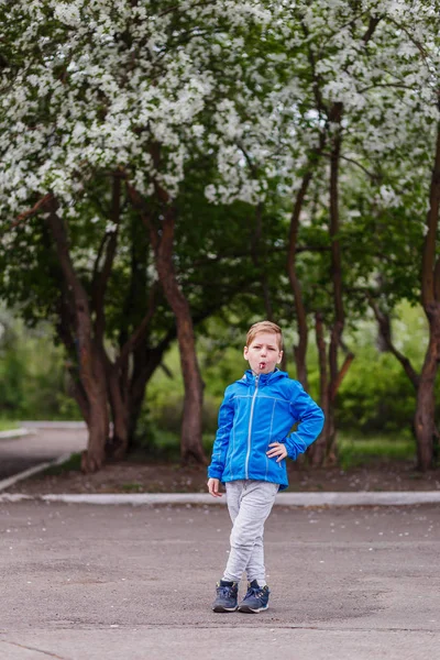 a six-year-old boy with a Lollipop in his mouth in full growth in the spring near a flowering Apple tree. spring bloom