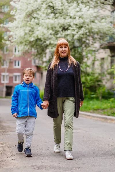 happy young grandma and a seven year old boy go together hand in hand in the city in the spring