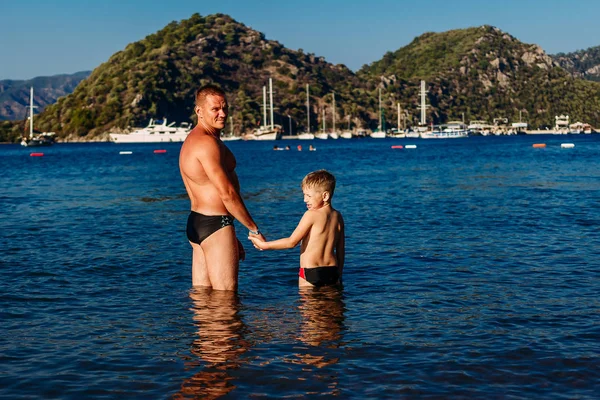 海で海で子供の手を握って男立っている彼の父を持つ少年 — ストック写真