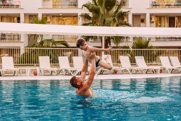 a man raises a child in the pool. Tanned happy father and son on vacation