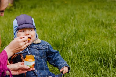 bir yaşındaki bebek bebek maması bir kaşık açık havada, yeşil ot yiyor