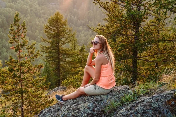 Длинноволосая загорелая задумчивая женщина сидит высоко в горах — стоковое фото