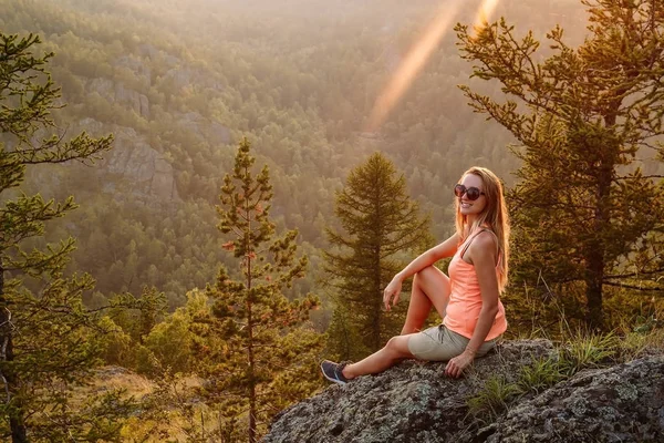 Улыбающаяся блондинка, сидящая на скале в горах под — стоковое фото