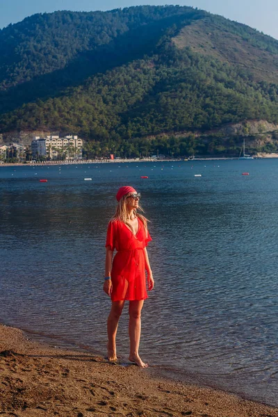 Стройная молодая женщина в красном пляжном тунике и бандане, гуляющая по морю, Турция — стоковое фото