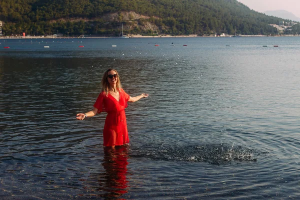 Ung kvinna i röd klänning på havets strand — Stockfoto