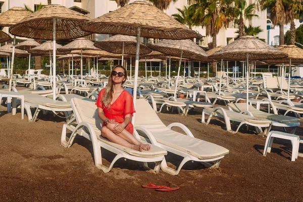 Сексуальная белая женщина в красной прозрачной пляжной тунике лежит на белом шезлонге на пляже — стоковое фото