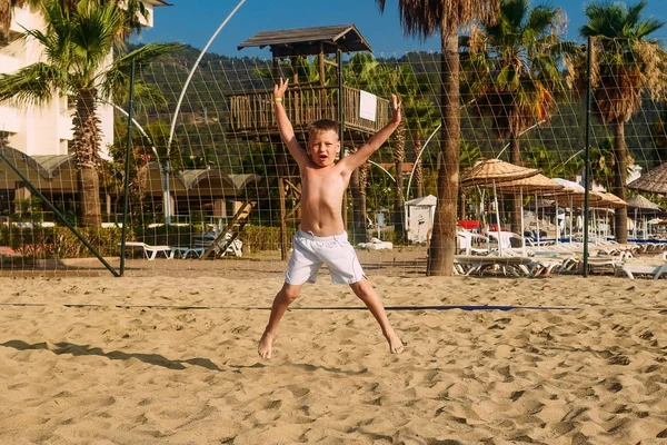 Menino caucasiano bronzeado em shorts brancos pulando na praia na areia na Turquia — Fotografia de Stock