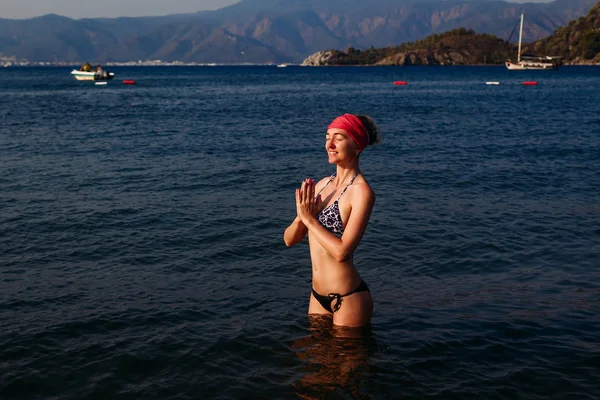 Trettio år gammal smal kvinna i en baddräkt och en bandana mediterar med knäppta händer på bröstet i Turkiet — Stockfoto