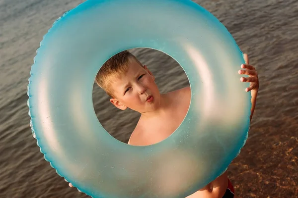 Загорелый шестилетний ребенок держит синий круг для купания летом в море — стоковое фото