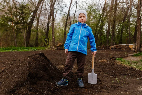 Семилетний мальчик с лопатой в саду — стоковое фото