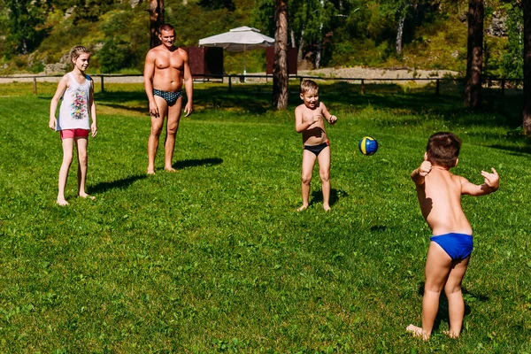 暑い夏の緑の芝生の上で、父親がボールを持って遊んでいる子供たち. — ストック写真